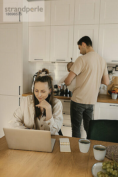 Frau arbeitet am Laptop in der Küche  Familie im Hintergrund zu Hause