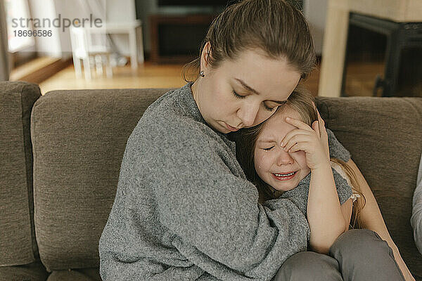 Mutter tröstet weinende Tochter auf Sofa