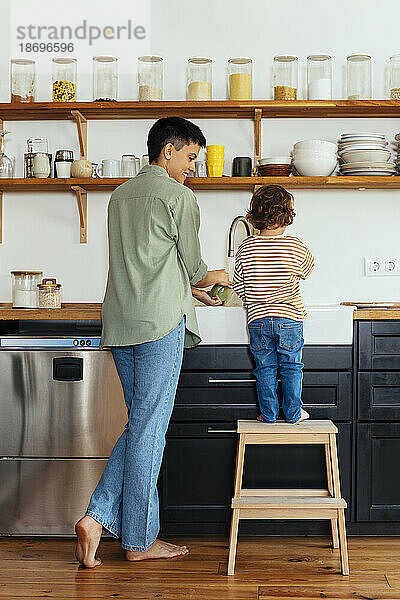 Woman doing dishes with son in kitchen at home
