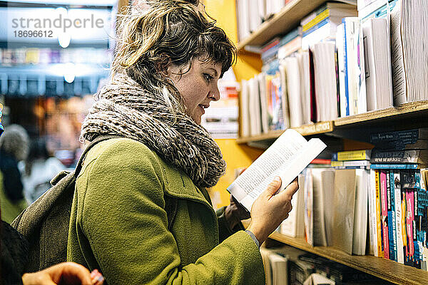 Frau mit Schal liest Buch in Bibliothek