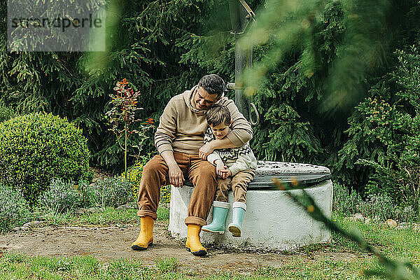 Vater und Sohn sitzen zusammen am Brunnen im Garten