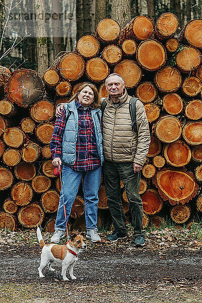 Älteres Paar mit Hund steht vor Kiefernstämmen im Wald