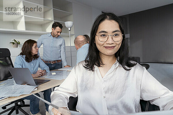 Selbstbewusste junge Geschäftsfrau mit Kollegen im Hintergrund im Büro