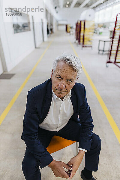 Serious businessman sitting on chair in factory