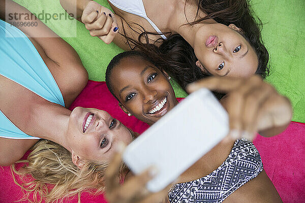 Smiling woman taking selfie with friends lying on colorful blanket