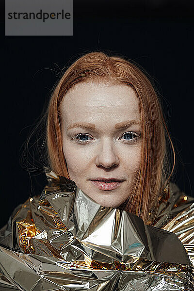 Redhead woman wrapped in foil against black background