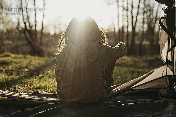 Mädchen schaut an einem sonnigen Tag vom Zelt aus auf den Wald