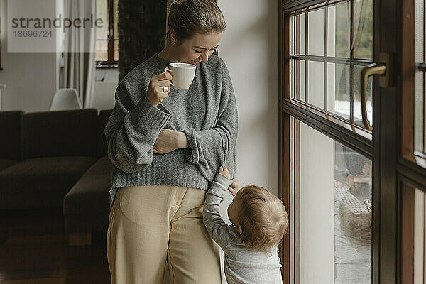 Sohn steht mit Mutter und hält Kaffeetasse zu Hause