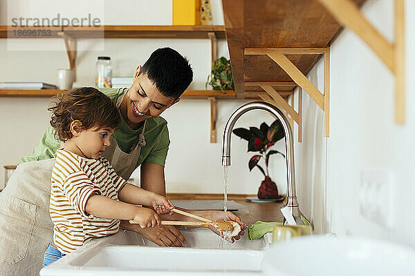 Sohn wäscht mit Mutter in der heimischen Küche Schöpfkellen im Spülbecken
