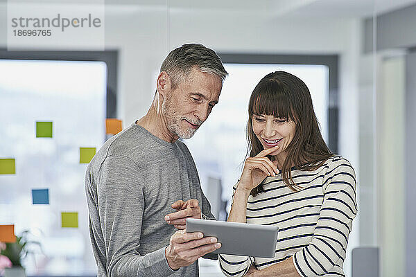 Geschäftsmann zeigt über Tablet-PC auf Kollegen im Büro