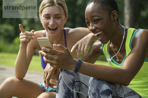 Fröhliche Freunde in Sportkleidung teilen sich im Park ihr Smartphone