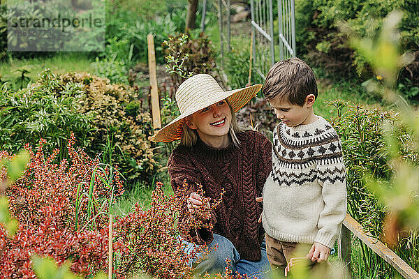 Lächelnde Mutter zeigt ihrem Sohn Blumen im Garten