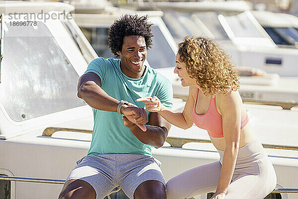 Mann zeigt Freundin  die am Hafen sitzt  Smartwatch