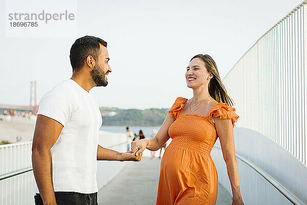 Smiling man enjoying with pregnant woman standing on footpath