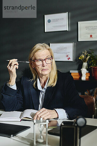 Nachdenklicher leitender Psychologe mit blonden Haaren sitzt am Schreibtisch im Büro