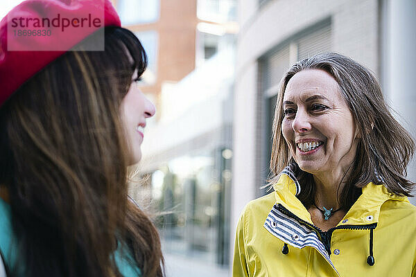 Lächelnde reife Frau im Gespräch mit einer Freundin vor dem Gebäude