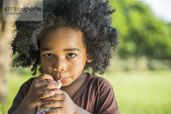Junge mit lockigem Haar nippt im Park an Getränk durch Strohhalm