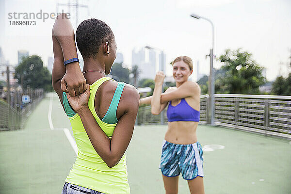 Woman in sports clothing stretching with friend on footpath