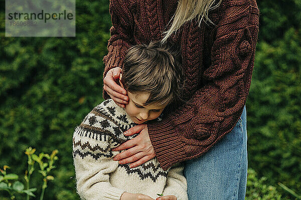Mother in brown sweater embracing son in garden