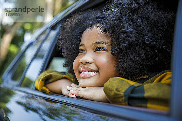 Lächelndes Mädchen träumt und lehnt sich an das Autofenster