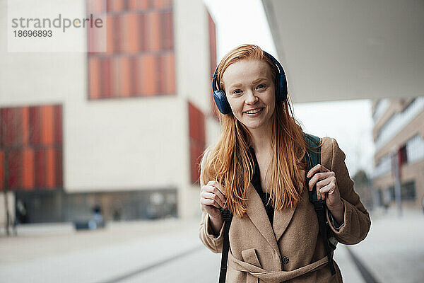 Lächelnde Frau mit Bluetooth-Kopfhörern vor dem Gebäude
