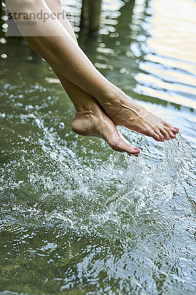 Frau spritzt mit Füßen Wasser in See