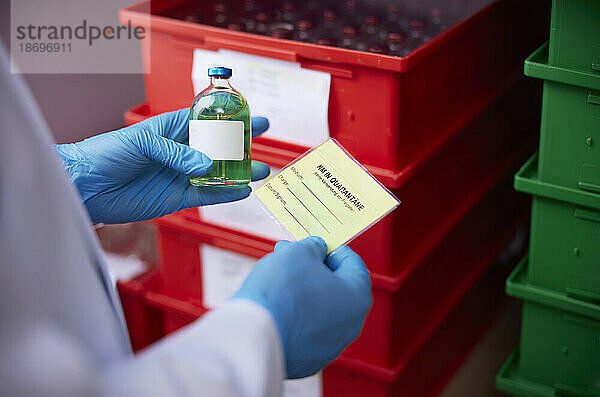 Hand eines Wissenschaftlers  der eine chemische Flasche im mikrobiologischen Labor untersucht