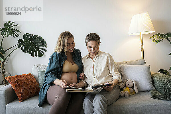 Mutter und schwangere Tochter teilen sich ein Fotoalbum  sitzen zu Hause auf dem Sofa
