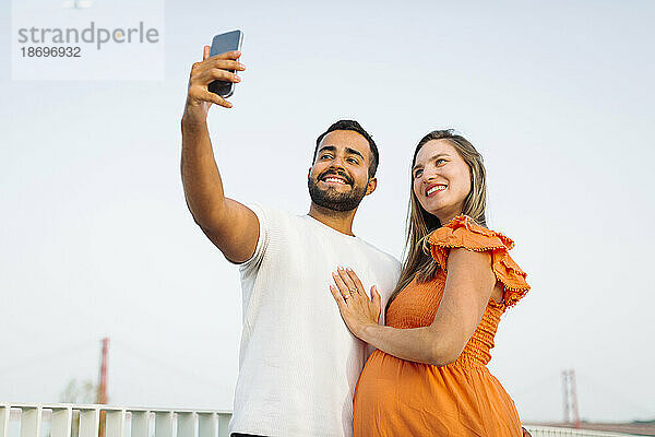 Lächelnder Mann macht Selfie mit schwangerer Frau
