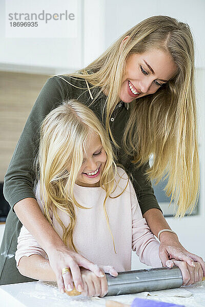 Glückliche Frau hilft ihrer Tochter beim Teigrollen in der heimischen Küche