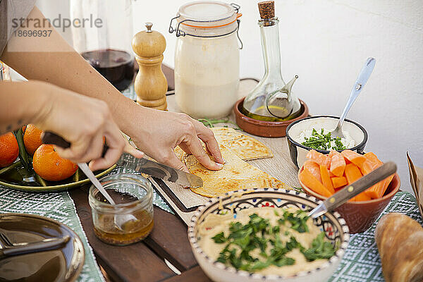 Hände schneiden fermentiertes Brot  umgeben von gesunden Mahlzeiten in Schüsseln und veganen Produkten