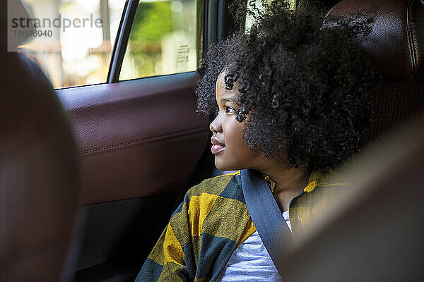Mädchen mit lockigem Haar schaut im Auto aus dem Fenster
