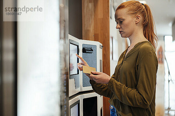 Rothaarige Frau bedient Geldautomaten
