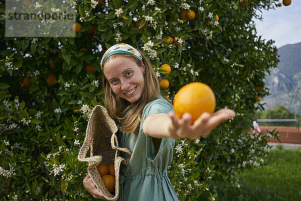 Glückliche Frau mit Orange in der Hand im Obstgarten