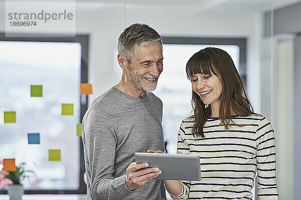 Geschäftsmann zeigt einem lächelnden Kollegen im Büro einen Tablet-PC