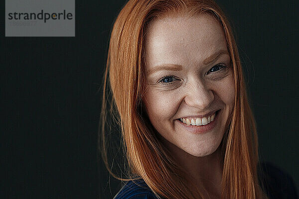 Cheerful redhead woman against black background