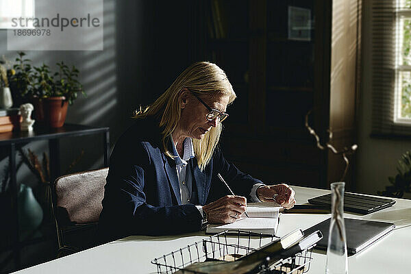 Blond senior psychologist preparing notes at desk in office