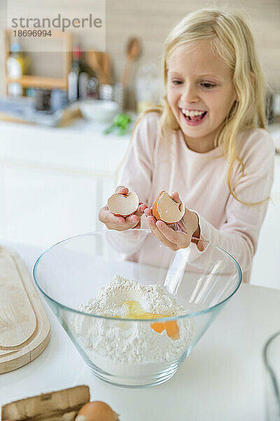 Glückliches Mädchen  das zu Hause in der Küche Eier in Mehl bricht