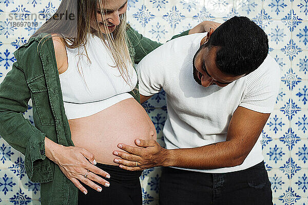 Mann berührt Bauch einer schwangeren Frau vor gefliester Wand