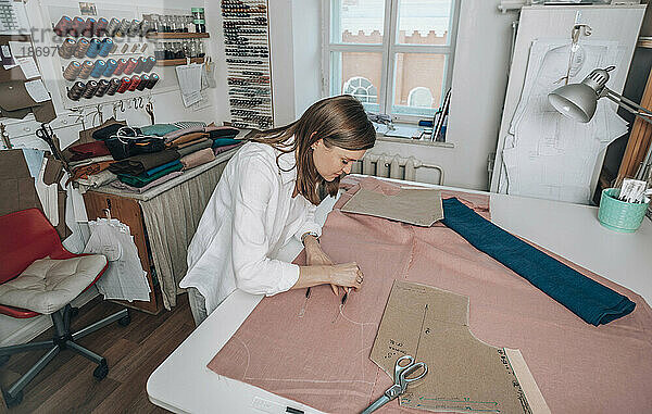 Modedesigner markiert Messungen auf Stoff in der Werkstatt