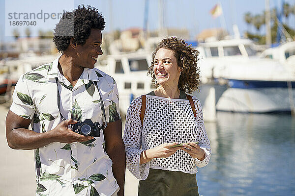 Fröhliches Paar mit Kamera beim Spaziergang am Hafen