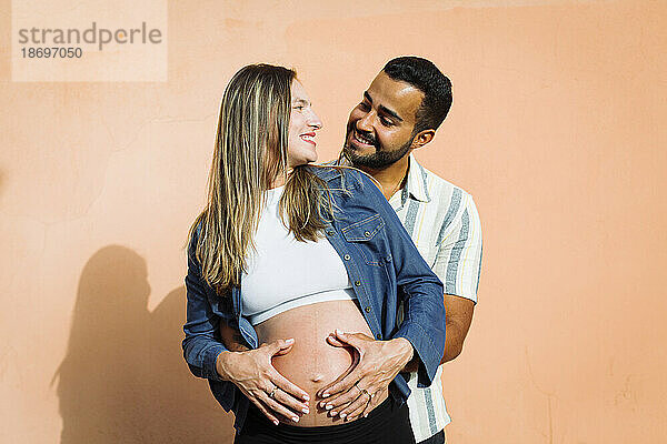 Happy couple with hands on stomach in front of wall