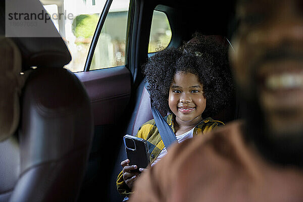 Lächelndes Mädchen mit Smartphone im Auto sitzend