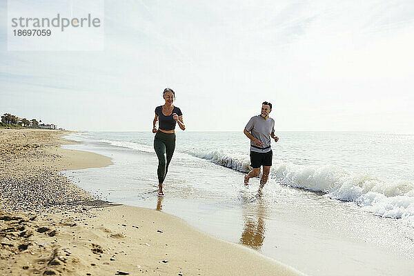Älteres Paar läuft gemeinsam durch die Welle am Strand