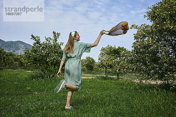 Frau spielt mit Netzbeutel auf Gras im Orangengarten