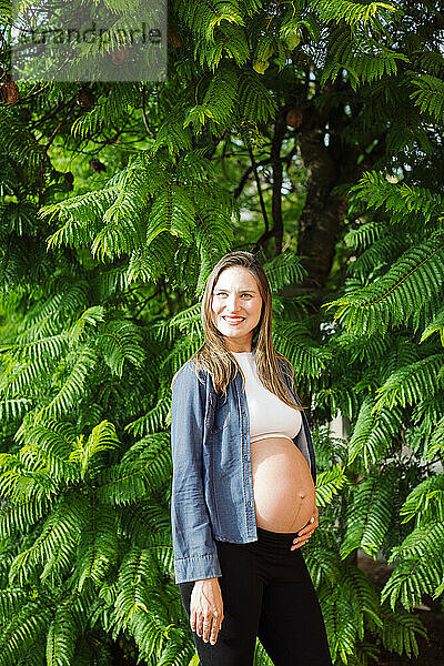 Lächelnde schwangere Frau  die vor einem Baum steht