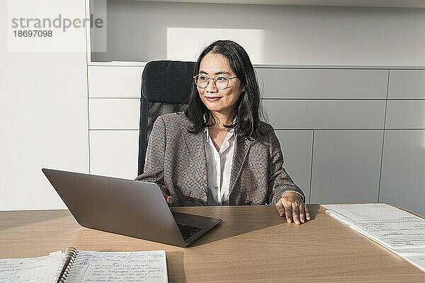 Thoughtful businesswoman sitting at desk in office with laptop