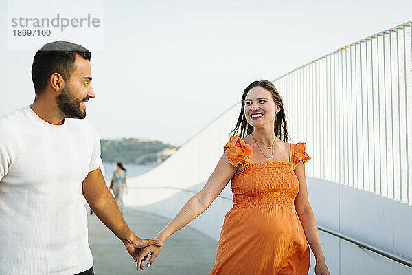 Happy pregnant woman holding hand of man at footpath