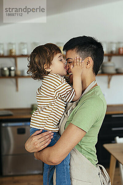 Sohn küsst Mutter in der heimischen Küche auf die Nase