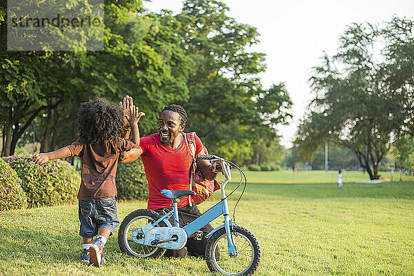 Vater gibt seinem Sohn im Park mit dem Fahrrad High-Five